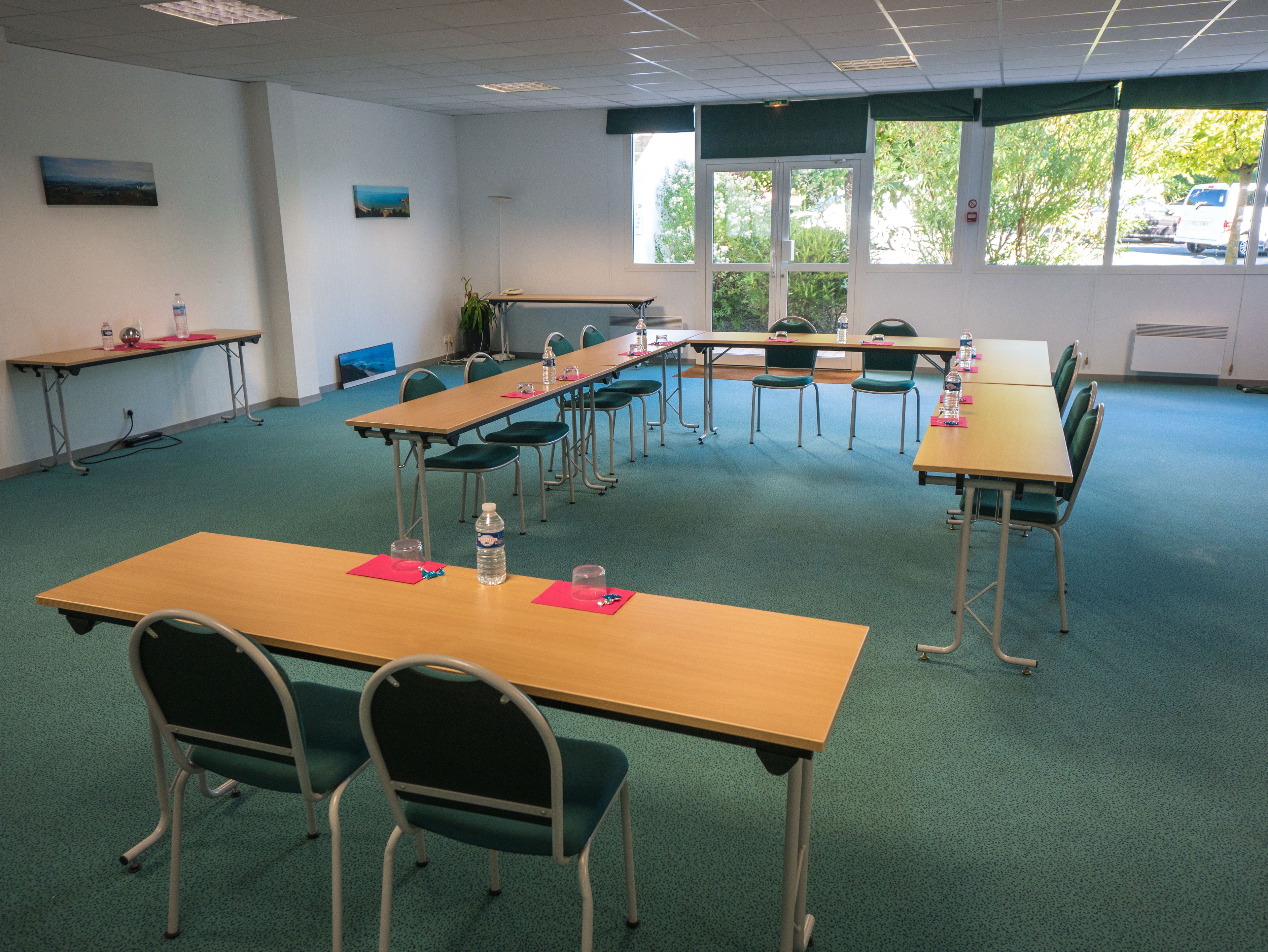 Uma sala de conferências com várias mesas e cadeiras, equipada com garrafas de água e blocos de notas.