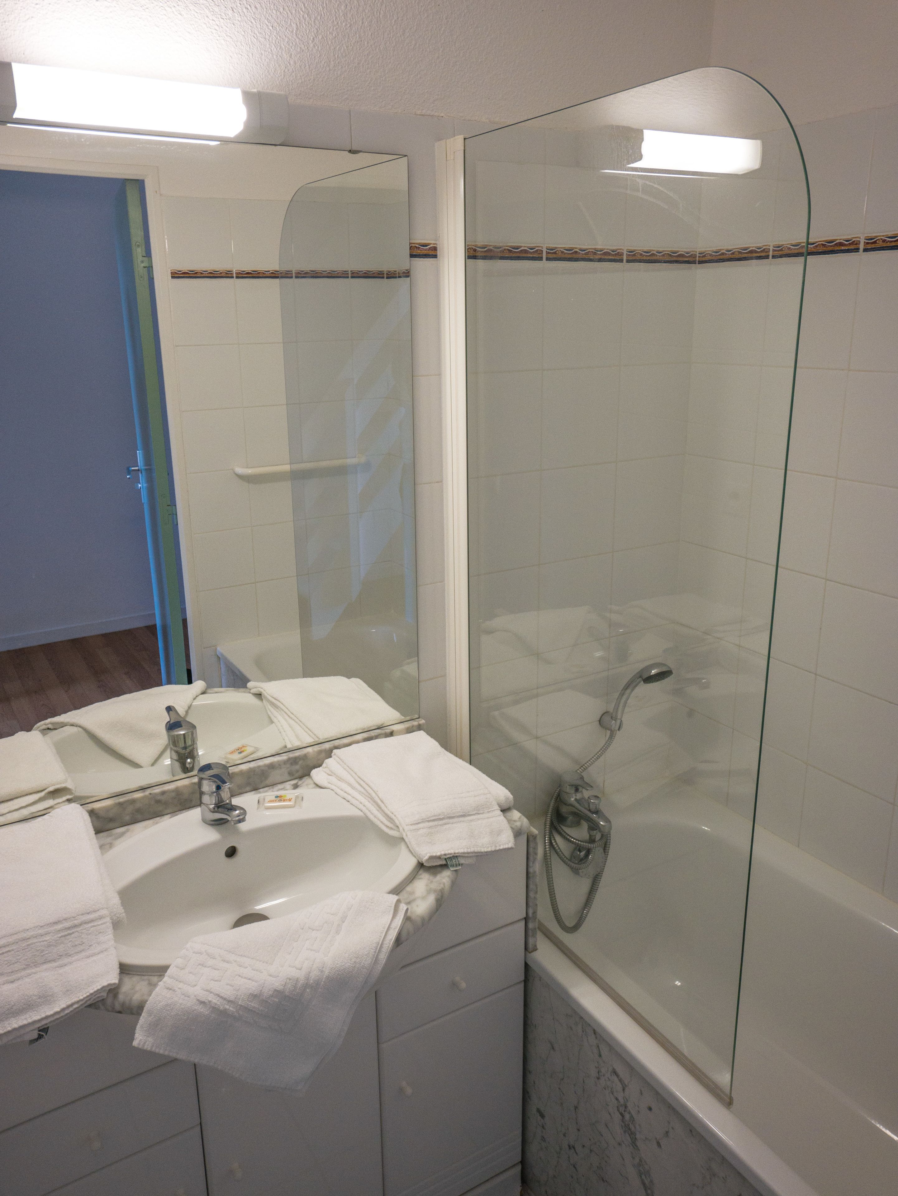 A bathroom with a glass-enclosed shower, a sink with a mirror, and a door leading to another room.