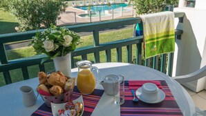 A table with breakfast items, a view of a pool, and greenery. - Résidence Ilbarritz (Bidart)