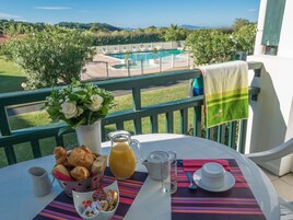 Una mesa con alimentos para el desayuno, vista a una piscina y follaje.