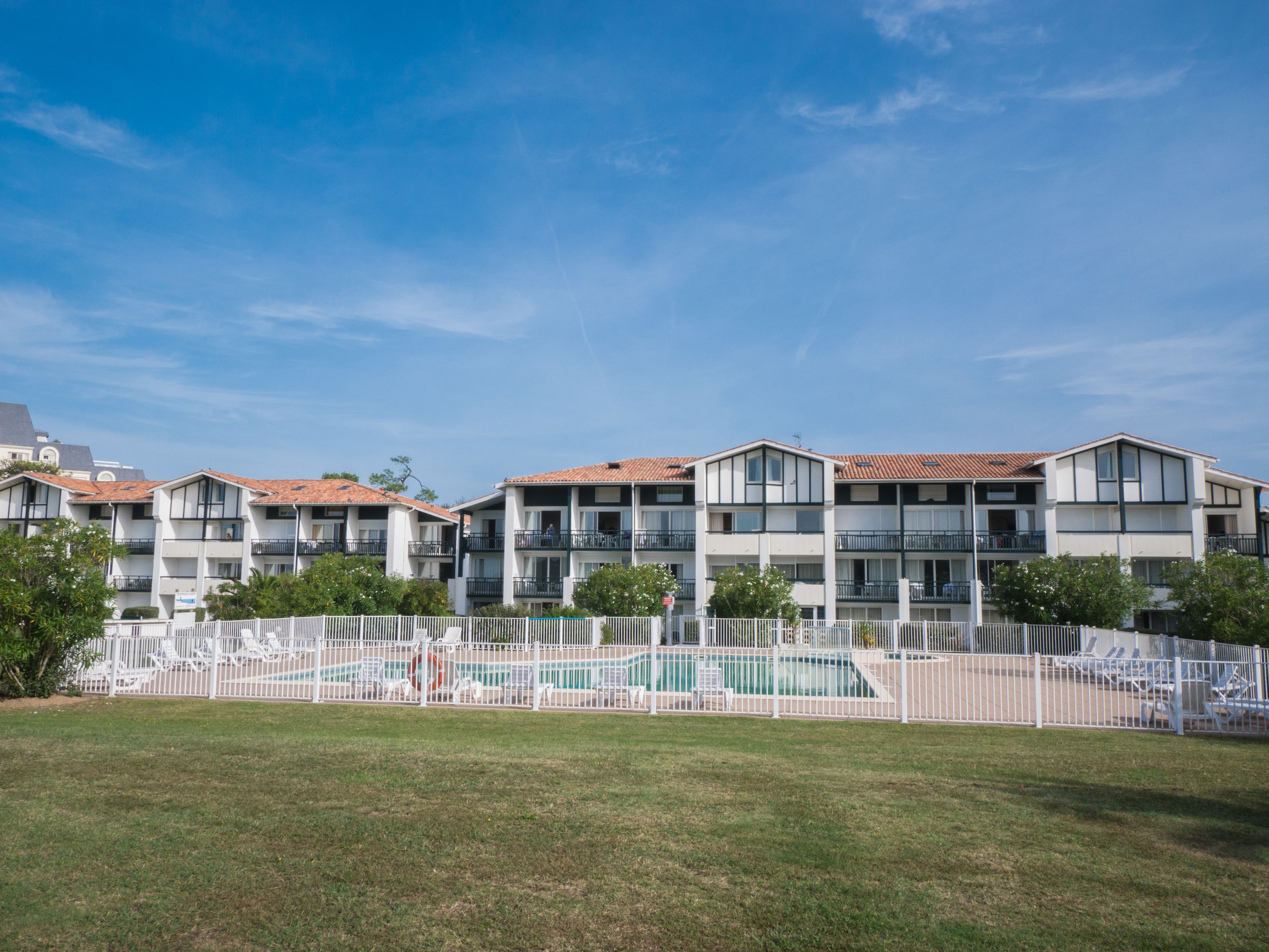 A multi-story hotel with balconies, a swimming pool, and a fenced outdoor area.