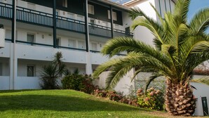 A multi-story hotel with balconies, a palm tree, and a well-maintained garden. - Résidence Ilbarritz (Bidart)