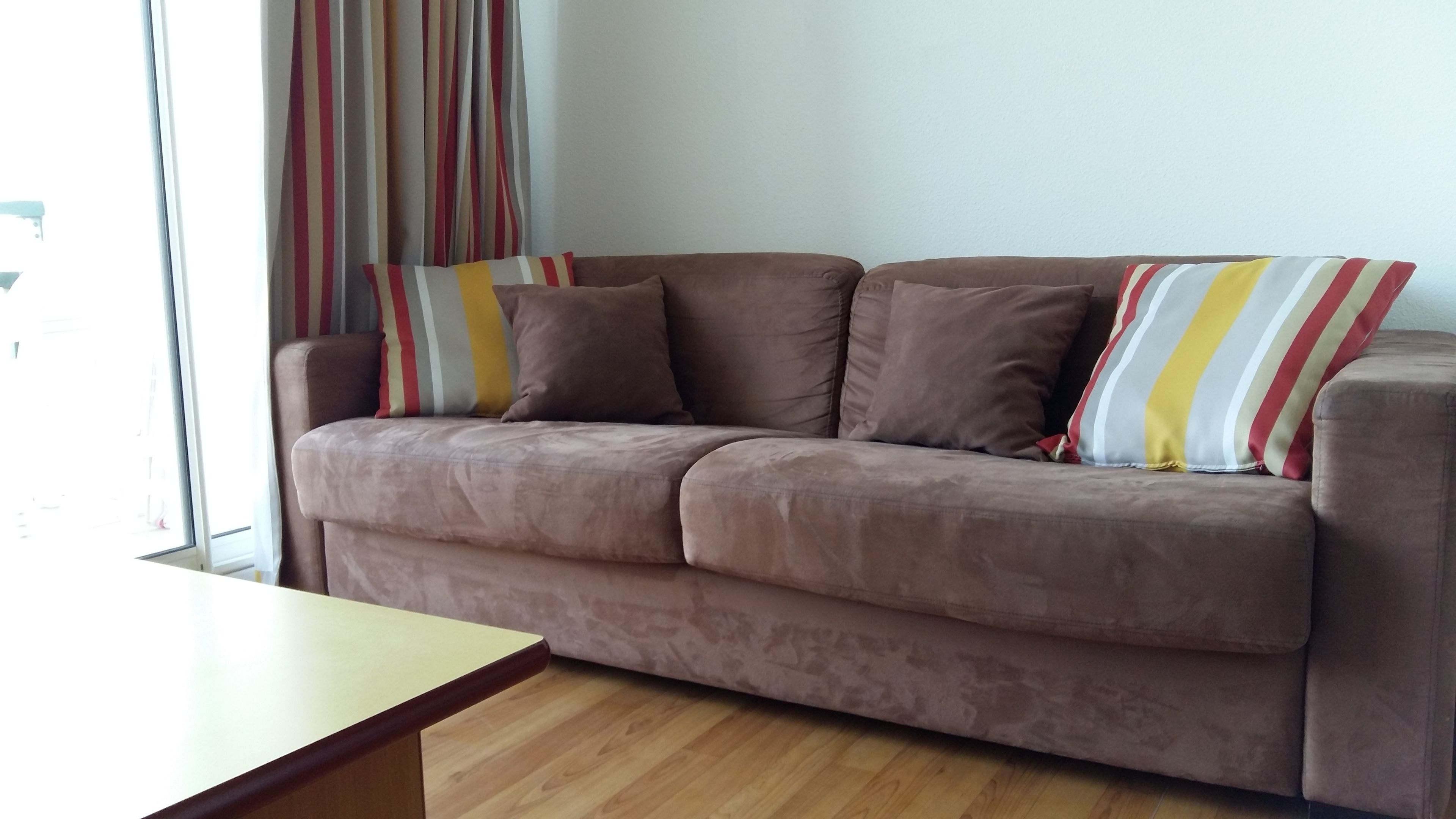 Ein braunes Sofa mit gestreiften Kissen, ein Couchtisch aus Holz und ein Fenster mit Vorhängen.