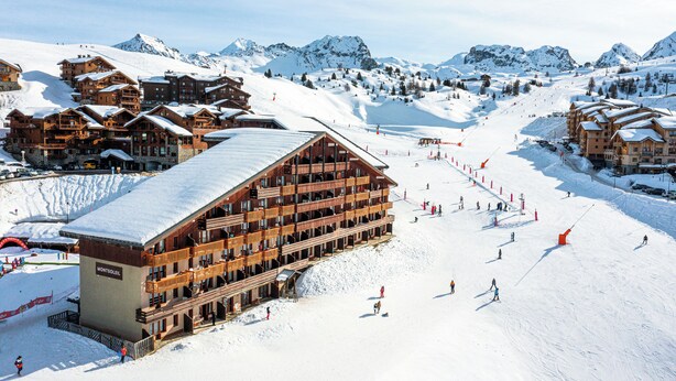A ski resort with multiple wooden lodges, a ski slope, and snow-covered mountains in the background.