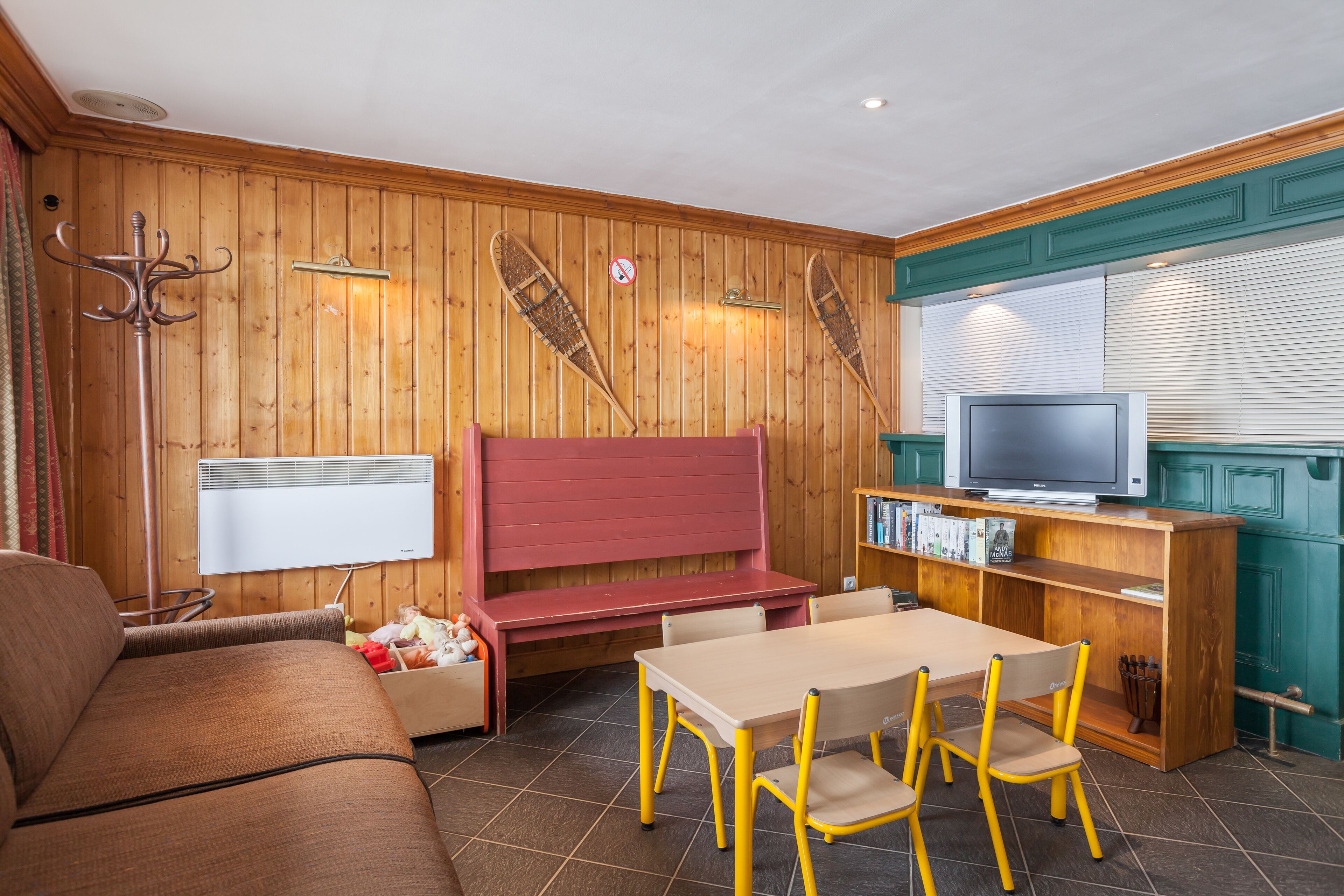 A cozy room with a wooden wall, a red bench, a TV, and a bookshelf.