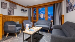 A cozy room with four grey upholstered chairs, a wooden coffee table, and a view of a snowy mountain at dusk.
