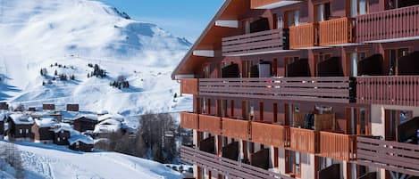 Ein mehrstöckiges Hotel mit Balkonen vor einer verschneiten Berglandschaft.