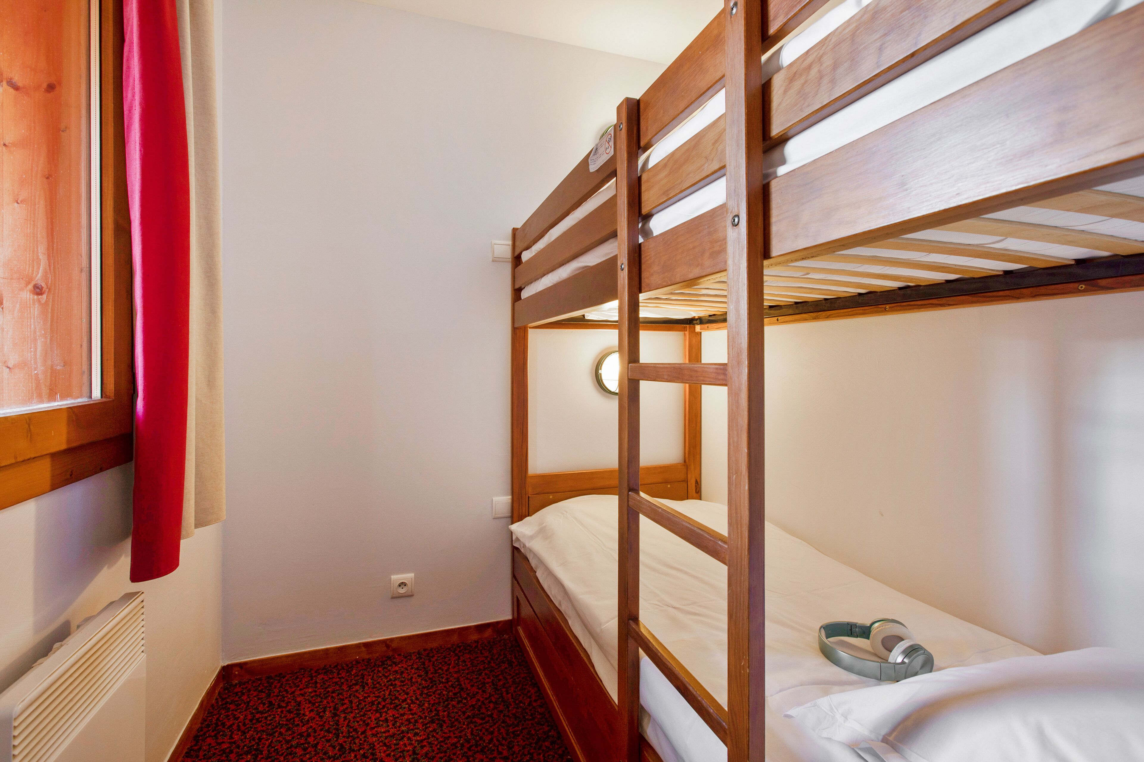 Habitación con literas, una cortina roja, una mesita con un cuenco y un reloj de pared.
