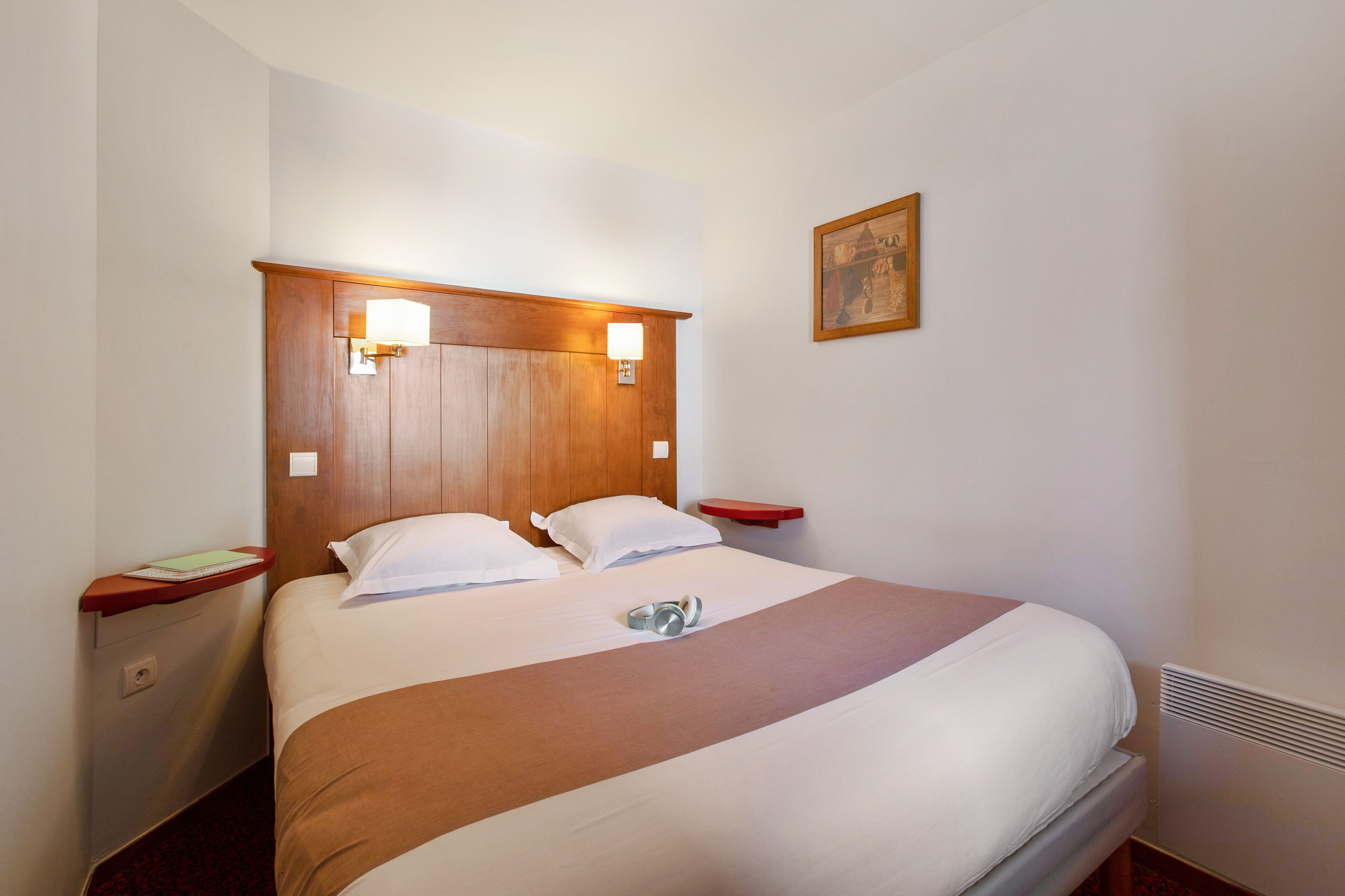 A hotel room with a large bed, wooden headboard, bedside tables, and a wall-mounted picture.
