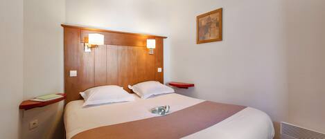 A hotel room with a large bed, wooden headboard, bedside tables, and a wall-mounted picture.