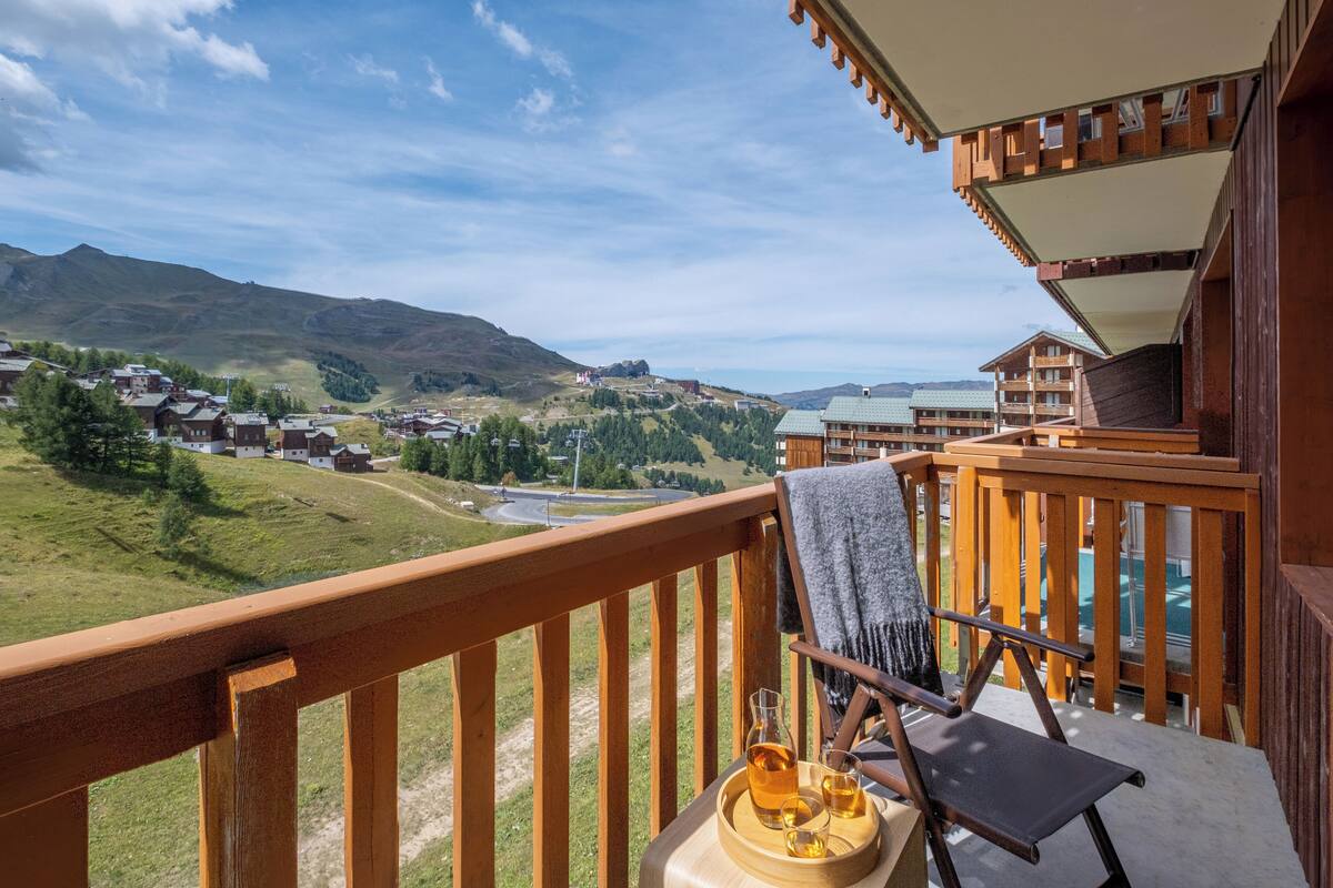 A balcony with a wooden railing, a chair, a towel, and a tray with a bottle and glass.