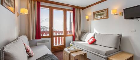 A hotel room with a sofa, a small table, a TV, and a window with curtains.