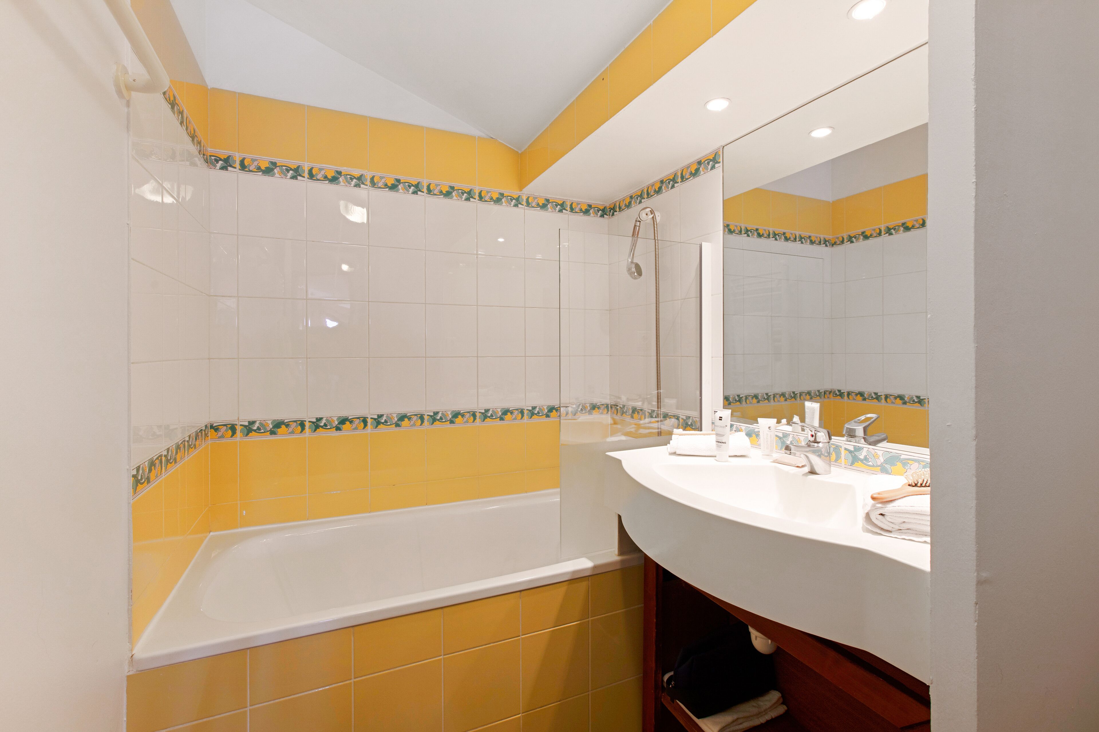 A bathroom with yellow and white tiles, a bathtub, a sink, and a mirror.
