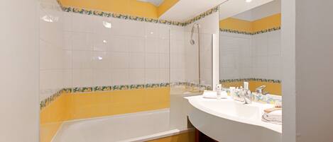 A bathroom with yellow and white tiles, a bathtub, a sink, and a mirror.
