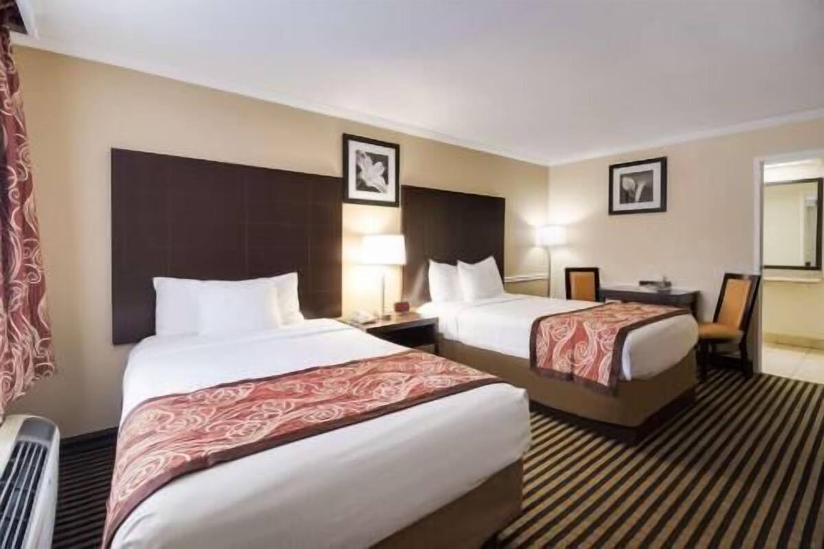 A hotel room with two beds, a nightstand, a lamp, and a mirror.
