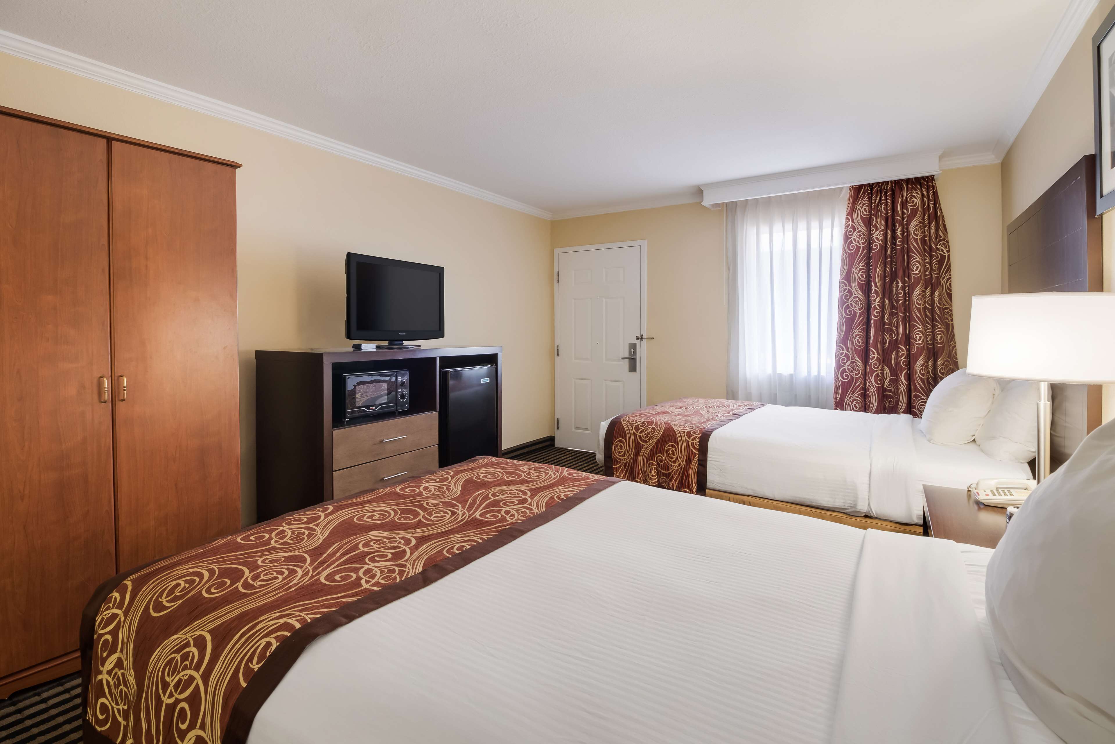 A hotel room with two beds, a television, a desk with a phone, and a wardrobe.