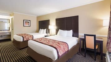 A hotel room with two beds, a desk, a chair, a lamp, and a bathroom visible through an open door.