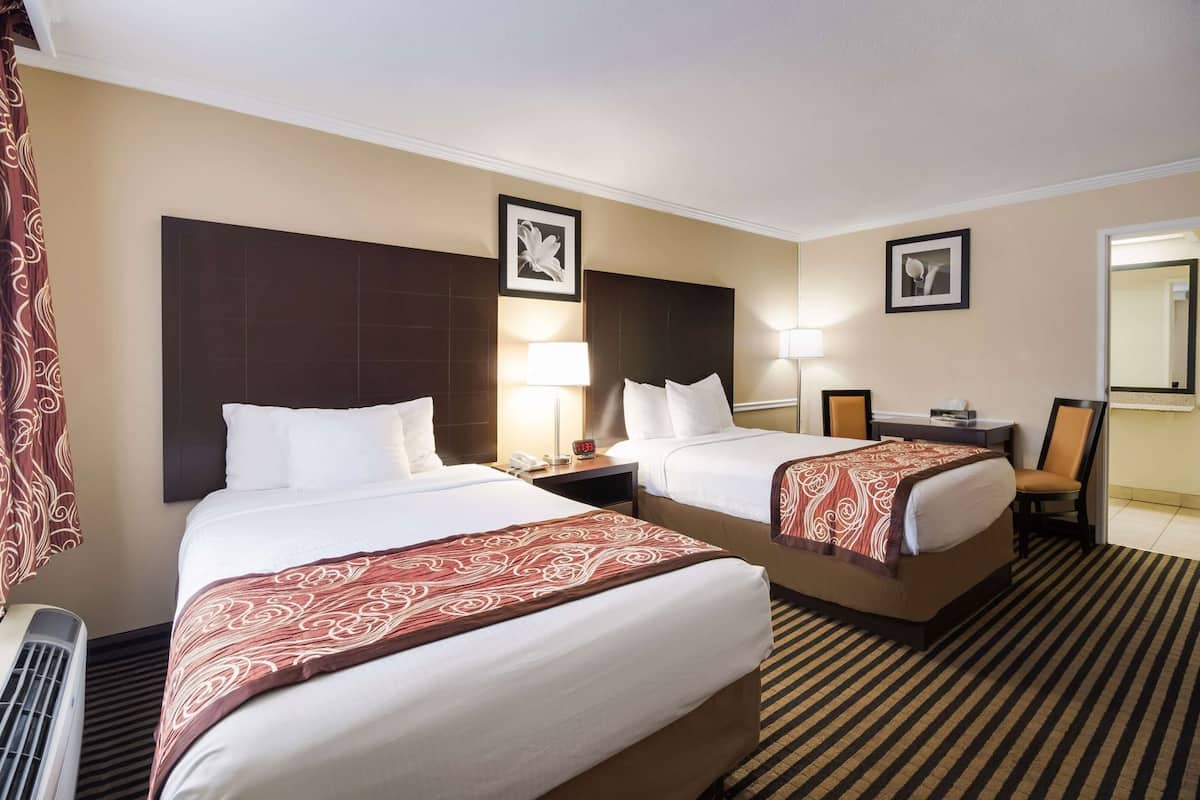 A hotel room with two beds, a desk, a chair, a nightstand, a lamp, and a picture frame on the wall.