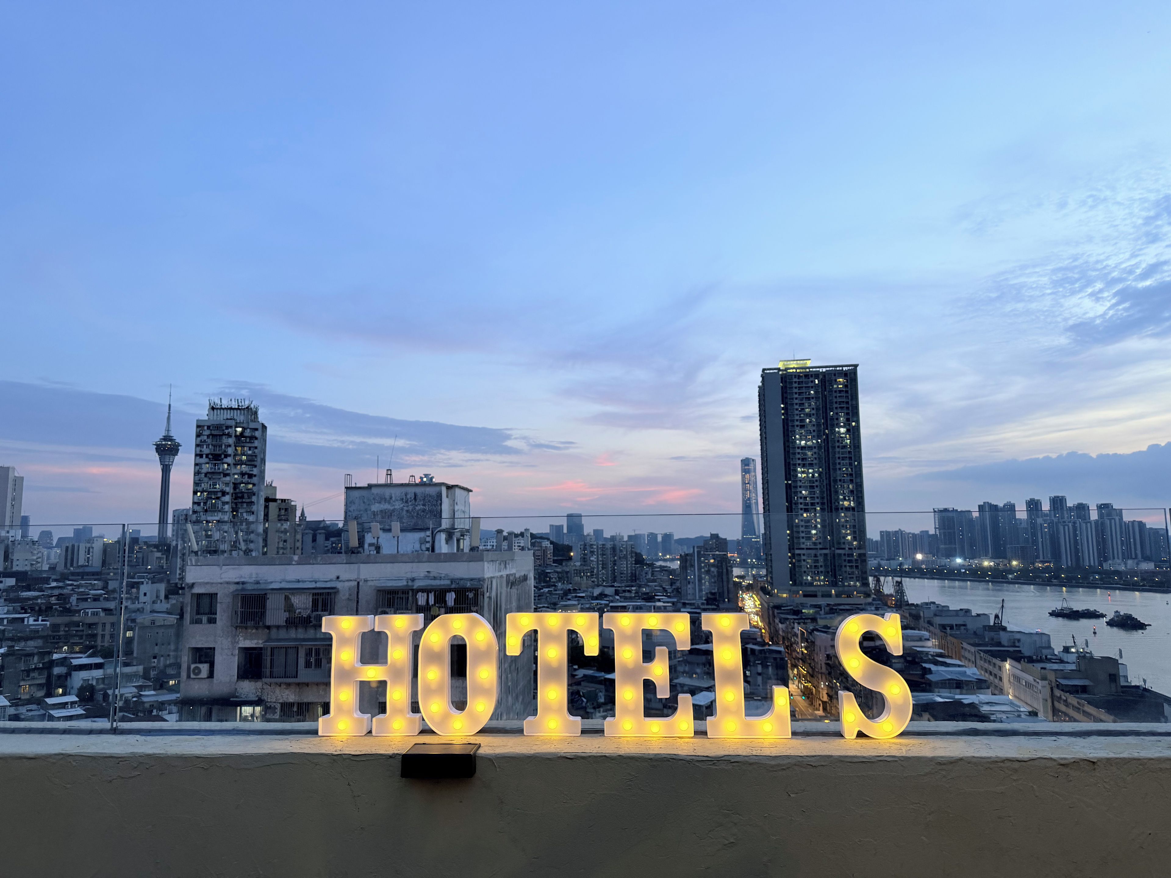 Une vue urbaine avec une enseigne lumineuse indiquant « HÔTELS », des immeubles de grande hauteur et une rivière.