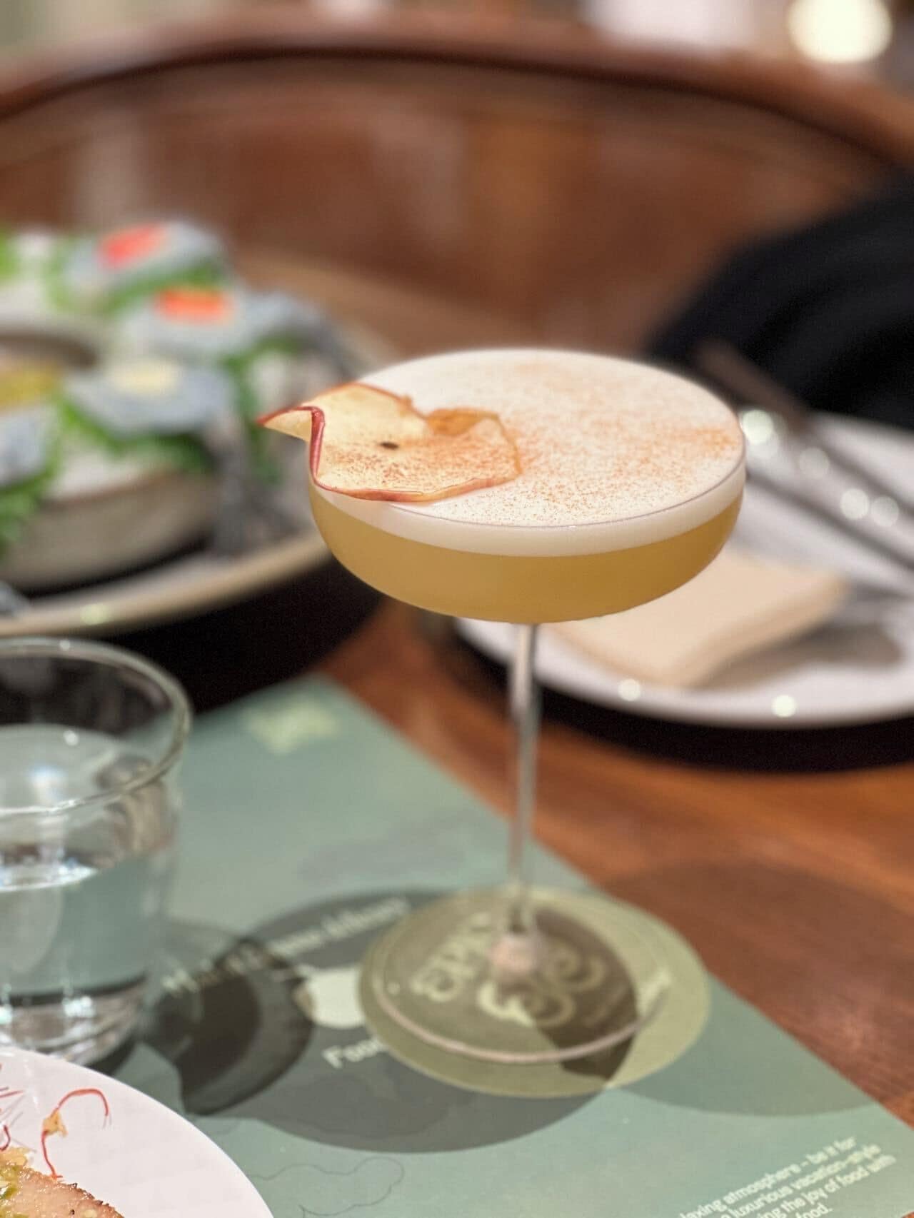 A cocktail glass with a frothy top, placed on a table with a menu underneath.