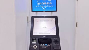 A self-service check-in kiosk with a monitor displaying instructions in multiple languages, a passport reading area, and a luggage tag dispenser.