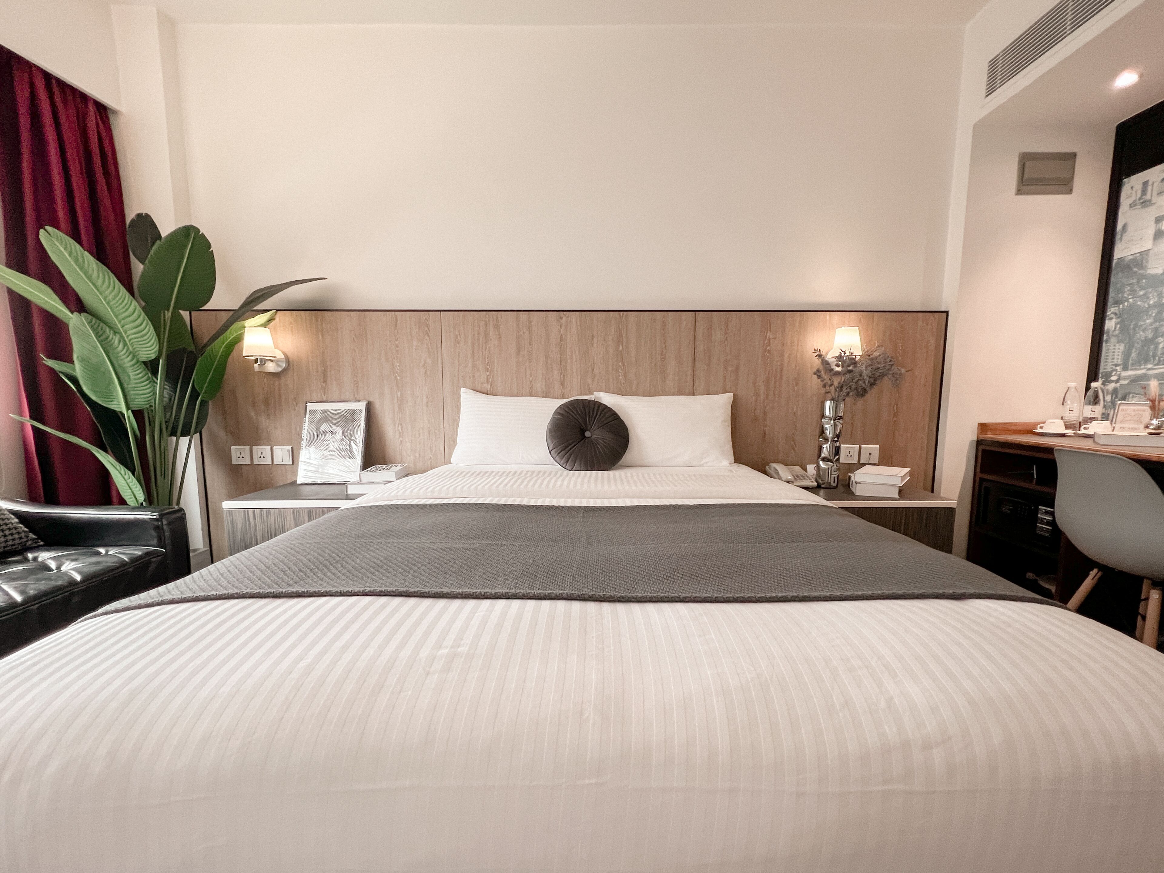 Ein Hotelzimmer mit einem großen Bett, einem Schreibtisch, einem Sessel, einer Lampe und einer Pflanze.