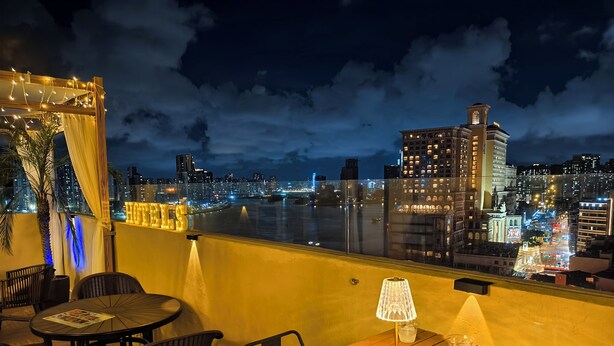 A rooftop terrace with a table and chairs, a lamp, and a view of a cityscape at night. - Macau Hotel S (Macau)