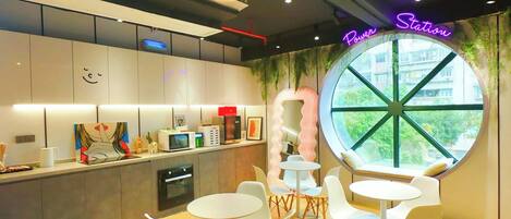 A modern cafe with round tables, white chairs, a large window with a view, and a neon sign reading 'Power Station.'