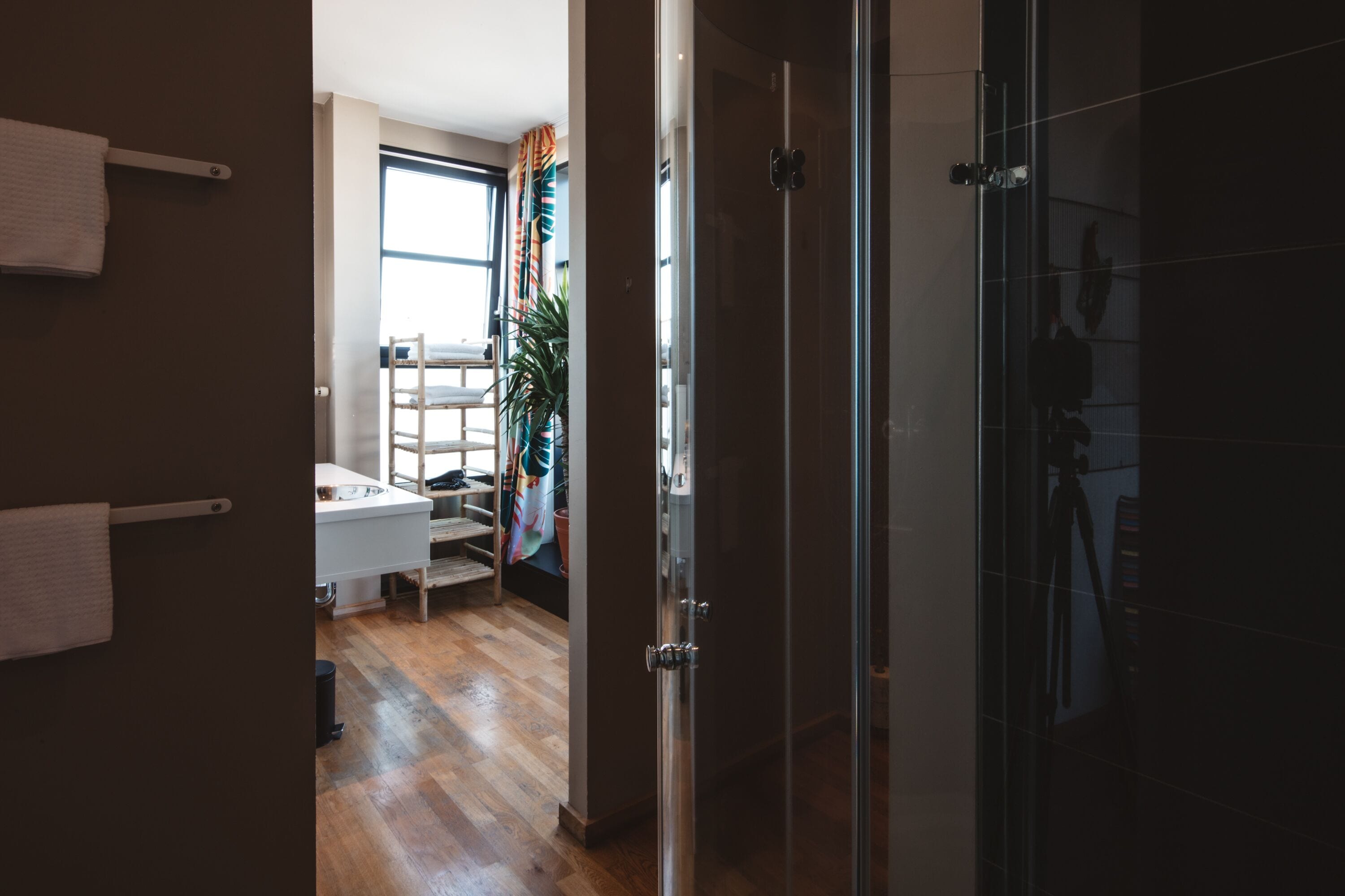 A modern bathroom with a glass shower enclosure, a white sink, and a wooden floor.