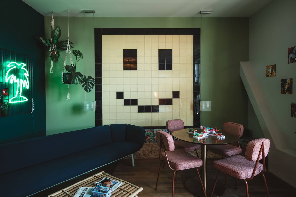 A room with a large wall mural, a neon palm tree sign, a sofa, and a dining table with chairs.