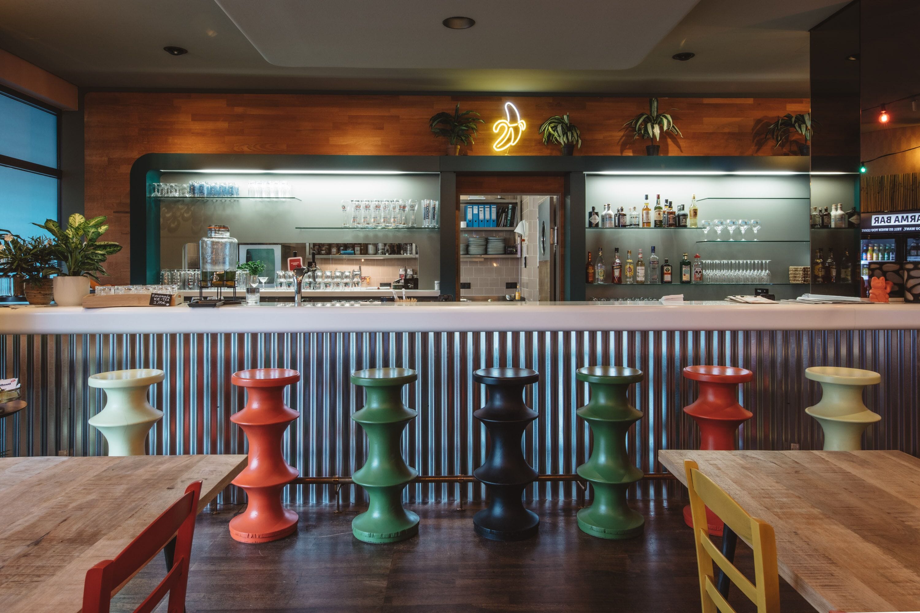 A bar area with stools, a wooden counter, and shelves with bottles and glasses.