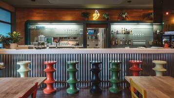 A bar area with stools, a wooden counter, and shelves with bottles and glasses.