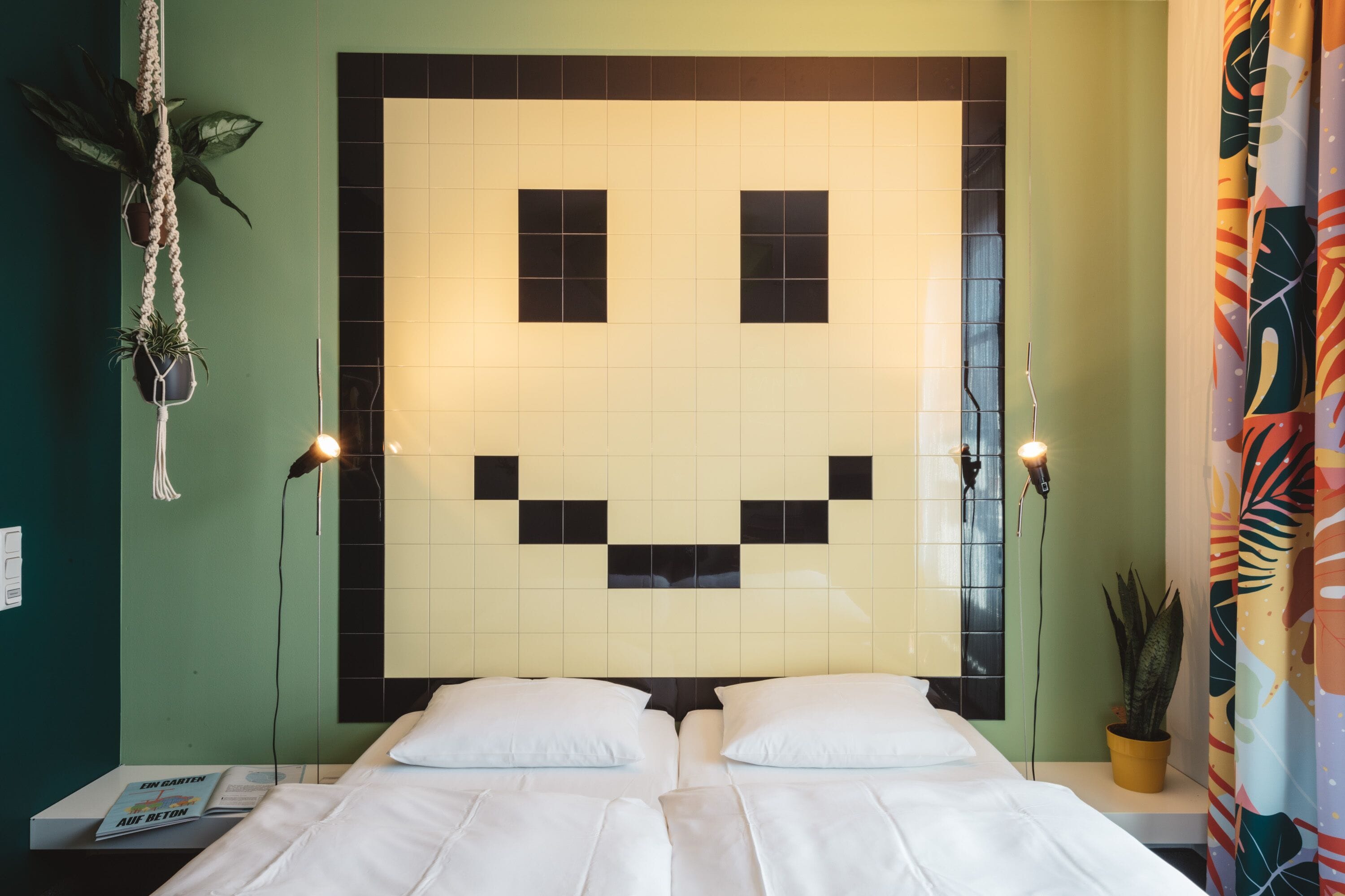 A room with a bed, two bedside tables, a wall with a smiley face design, and two potted plants.