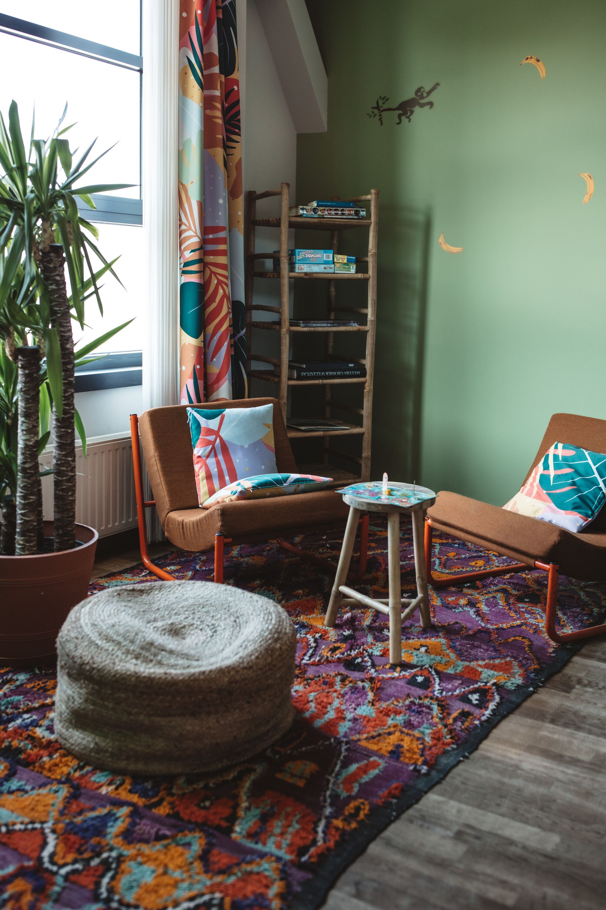 Une pièce chaleureuse avec une grande fenêtre, une plante en pot, un tapis coloré et une bibliothèque.