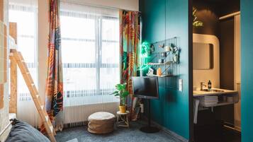 Habitación moderna con un ventanal amplio, televisión, planta y baño con lavabo y espejo.