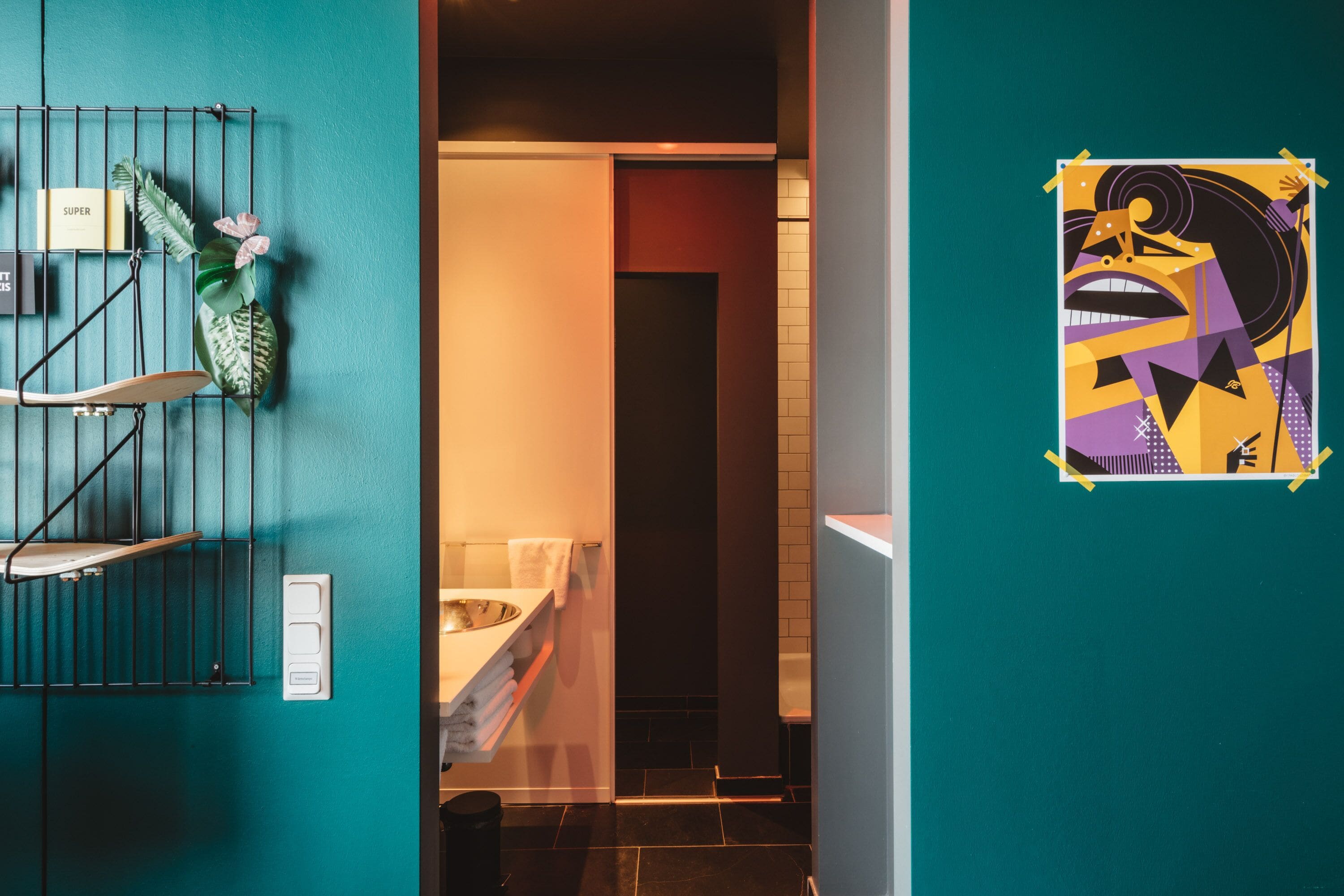 A modern bathroom with a teal wall, a metal rack with towels, and a poster on the wall.