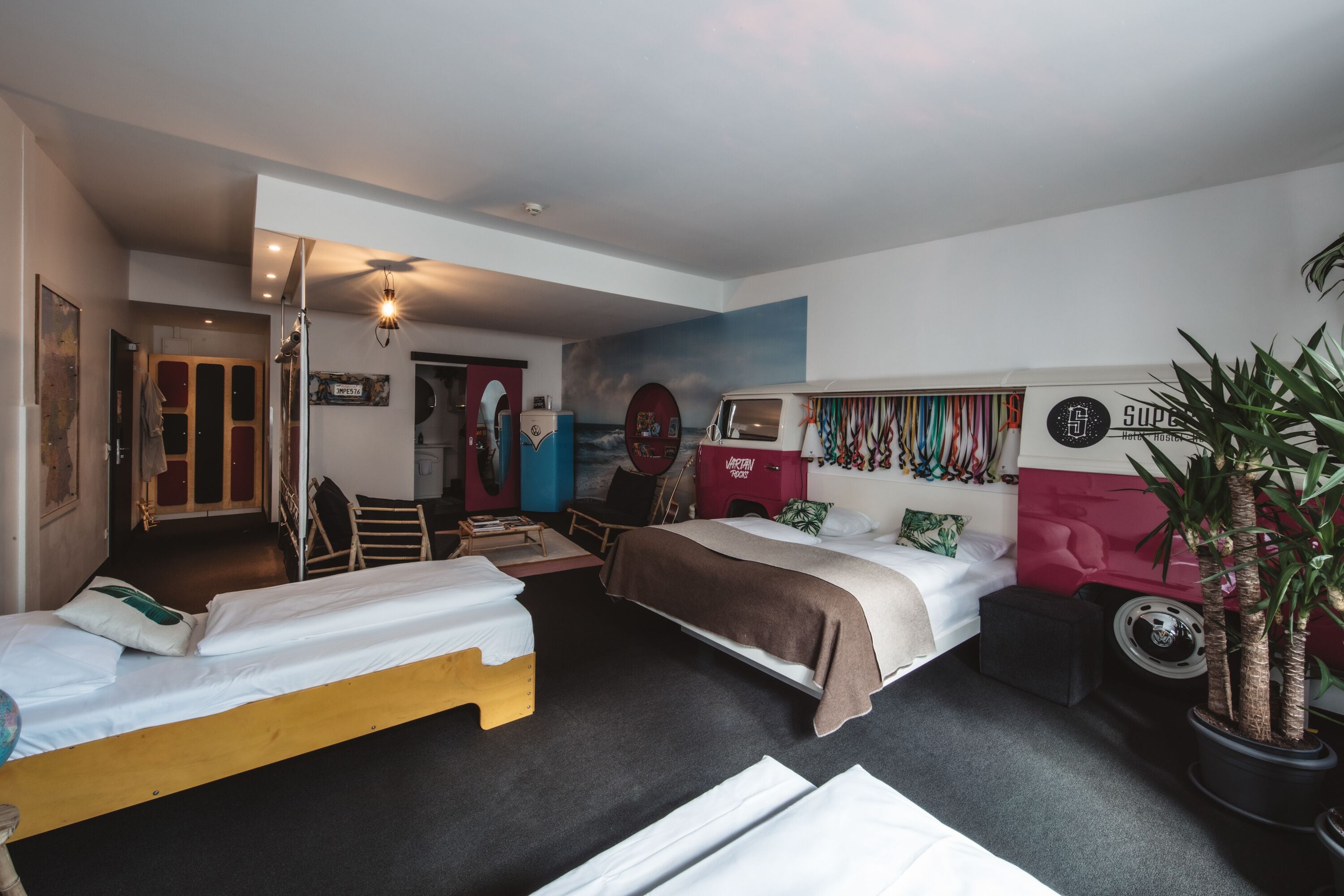 Een hotelkamer met twee bedden, een rode hoofdbord, een grote spiegel en een plant.