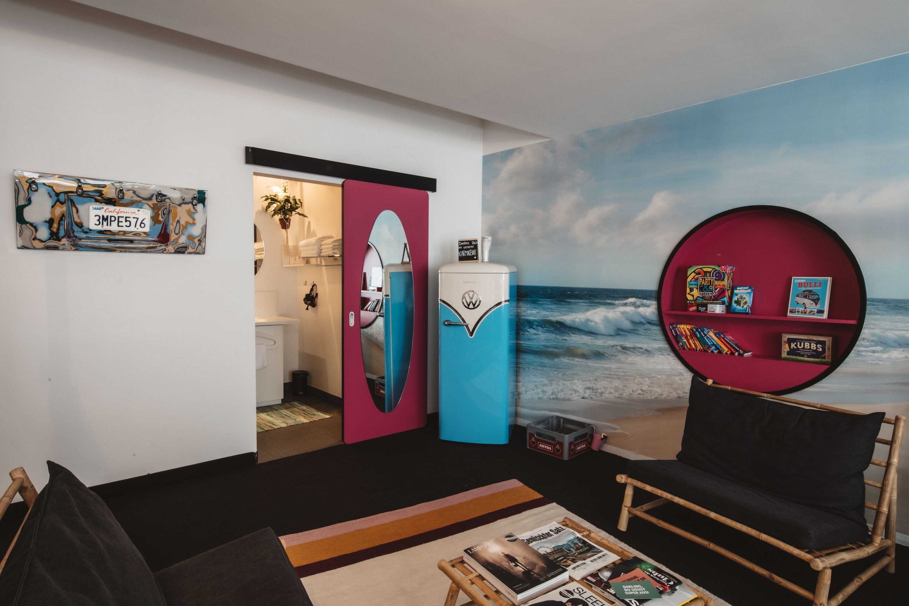 Une pièce décorée d’une fresque murale sur le thème de la plage, avec une planche de surf, une bibliothèque rouge et un canapé noir.