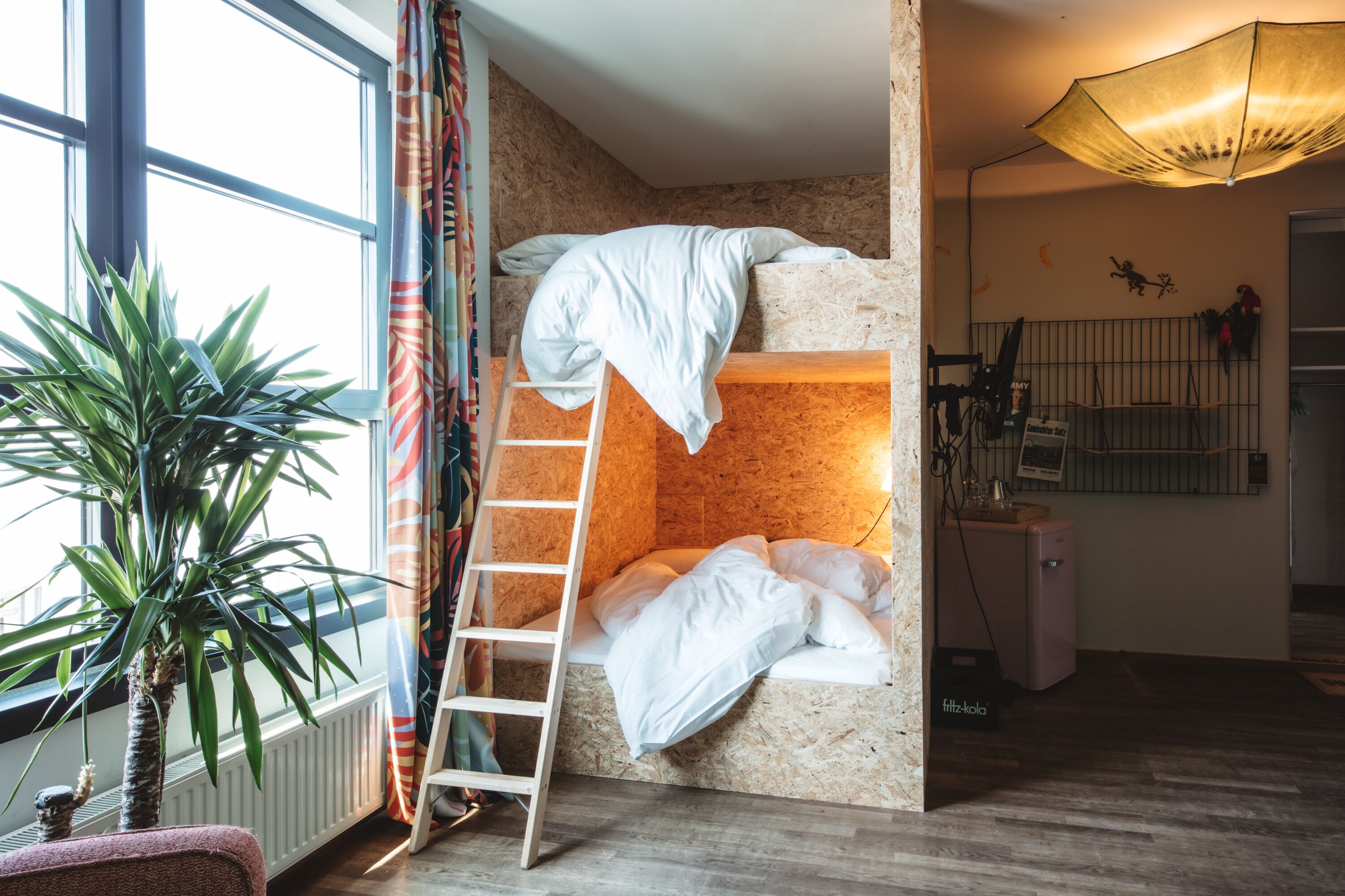 Een slaapkamer met een stapelbed, een trapje, een radiator, een kleine koelkast en een plant.