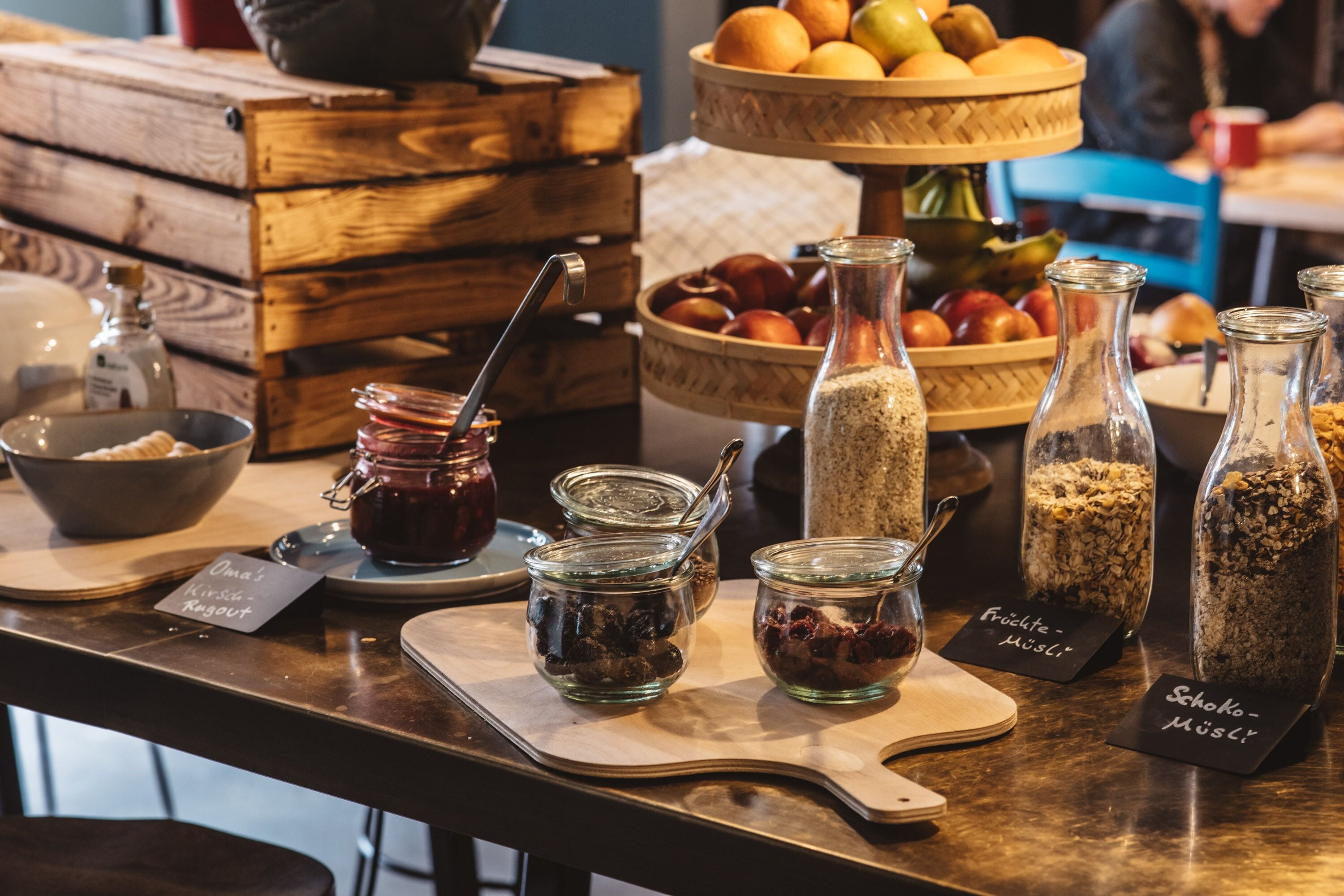 Ein Holztisch mit Gläsern mit Marmelade, einer Obstschale und einem Korb mit Brot.