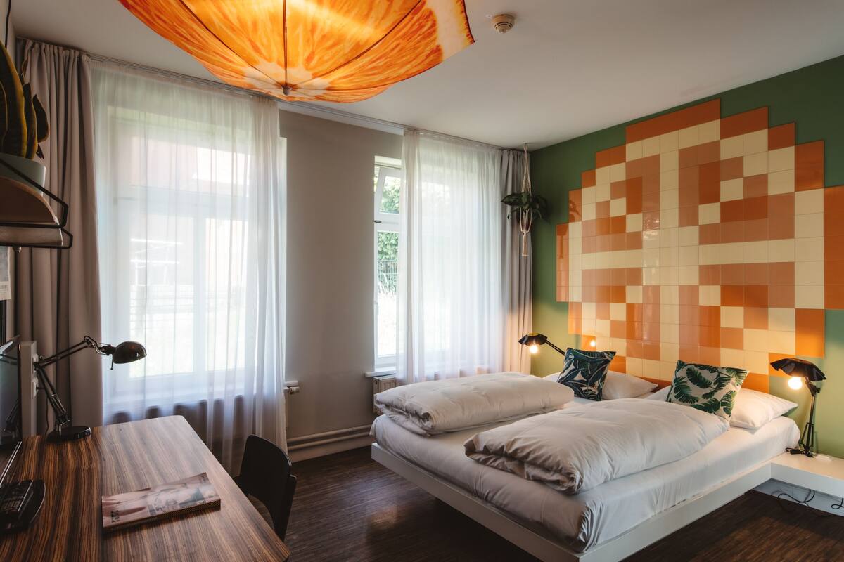 A bedroom with a bed, bedside lamps, a desk, and a window with curtains.