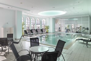 Un área de piscina interior moderna con paredes de vidrio, sillones de descanso y mesas.