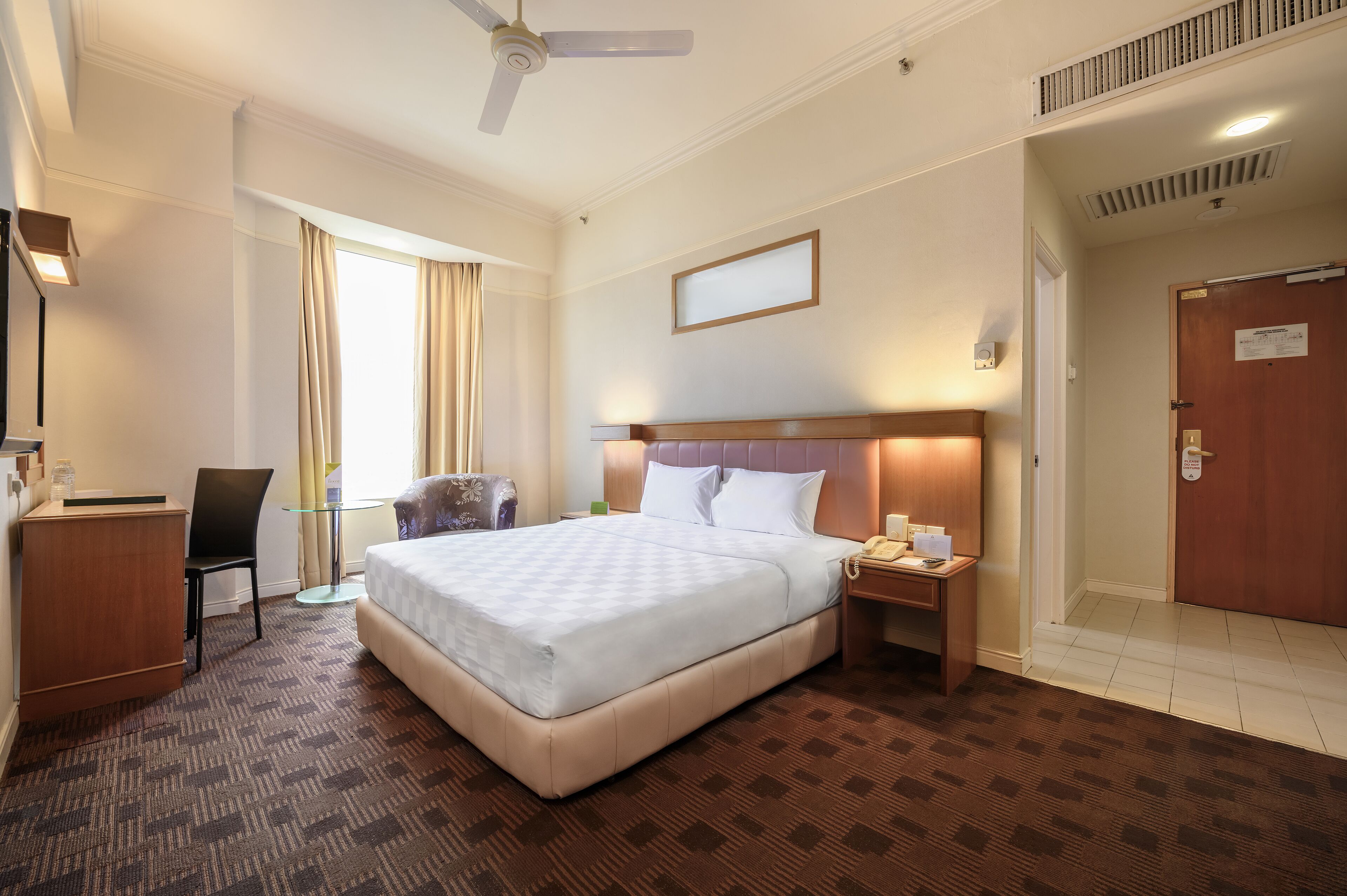 A hotel room with a bed, desk, chair, and a nightstand with a phone.