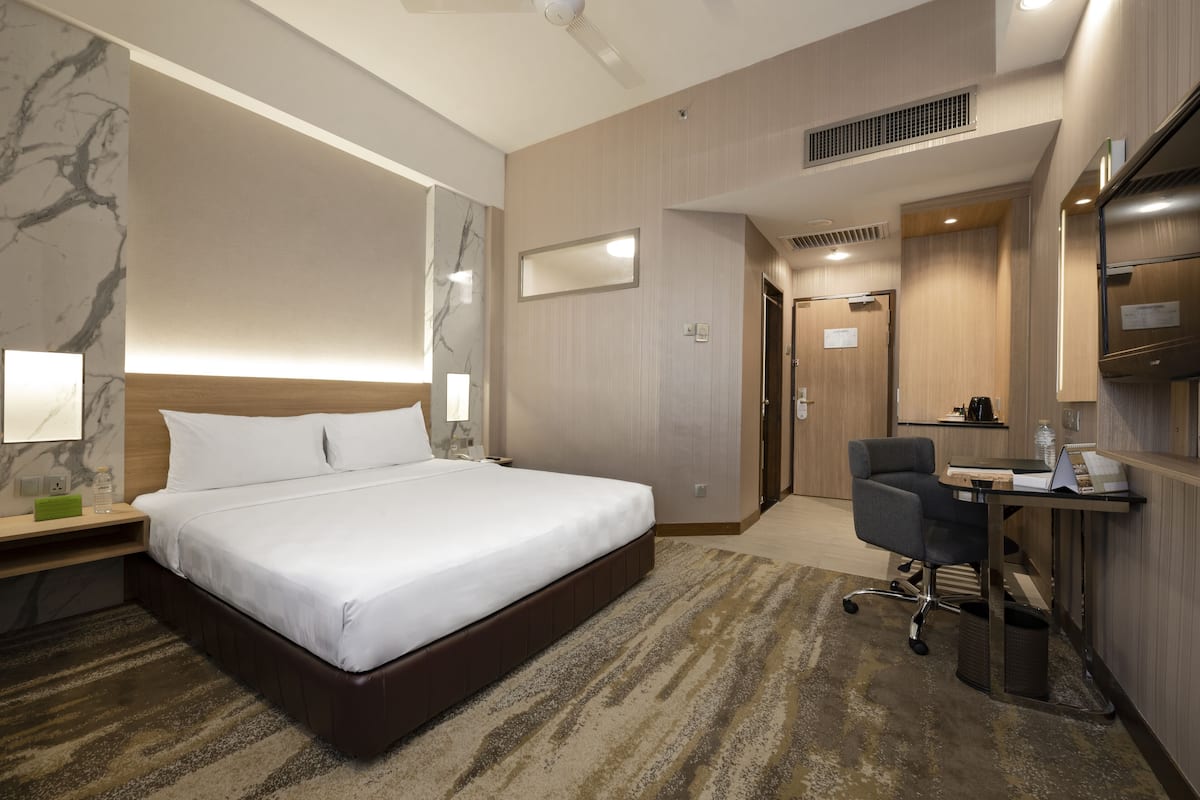 A hotel room with a large bed, a desk with a chair, a mirror, and a television.