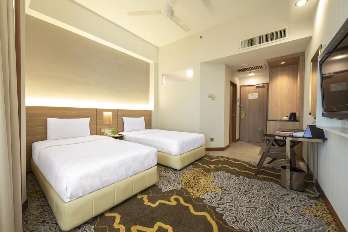A hotel room with two beds, a desk, a chair, a television, and a ceiling fan.
