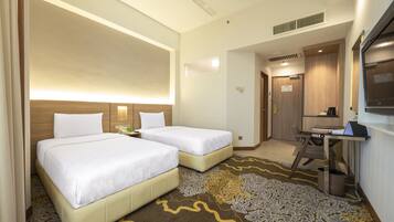 A hotel room with two beds, a desk, a chair, a television, and a ceiling fan.