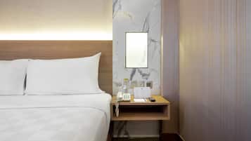 A hotel room with a bed, a wooden nightstand, a marble wall, a mirror, a phone, a water bottle, a notepad, and a remote control.
