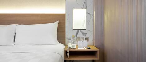 A hotel room with a bed, a wooden nightstand, a marble wall, a mirror, a phone, a water bottle, a notepad, and a remote control.