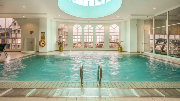 Una amplia piscina interior con tragaluces, varias ventanas y vistas a la ciudad.