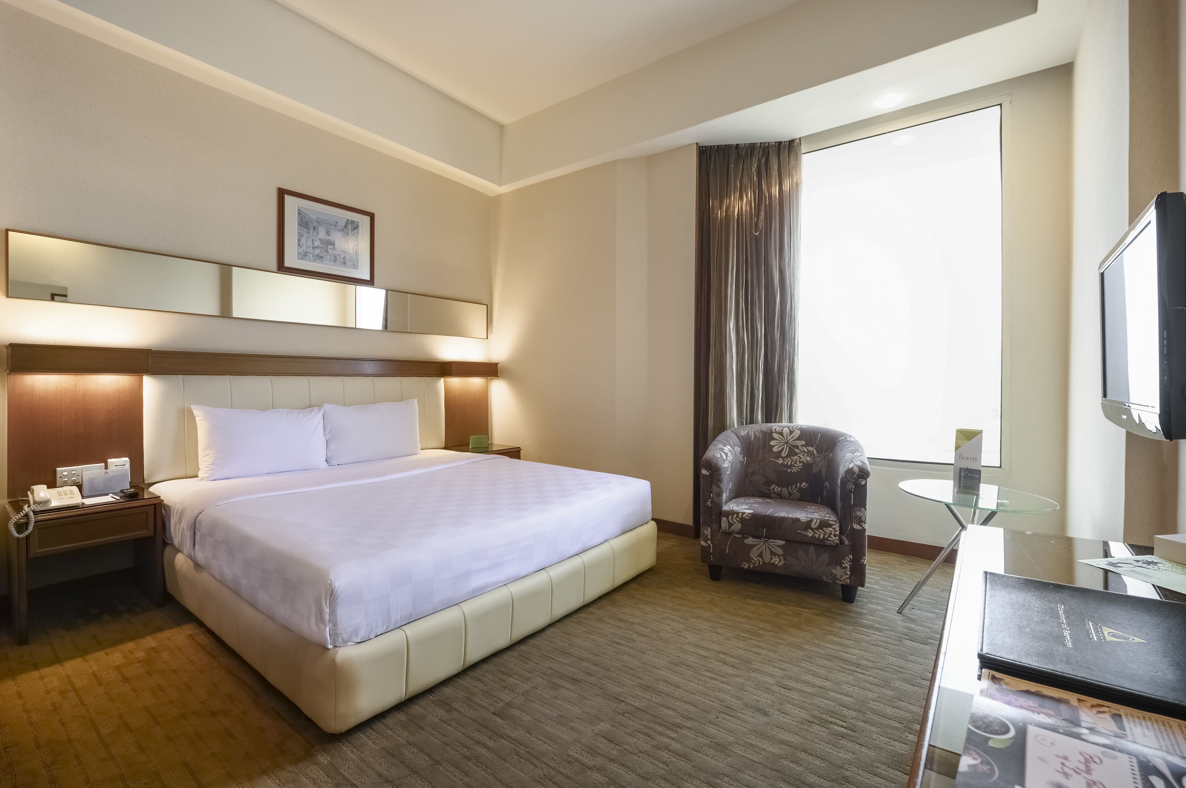 Une chambre d’hôtel avec un grand lit, une chaise, un bureau avec un ordinateur, un téléphone et une télévision.